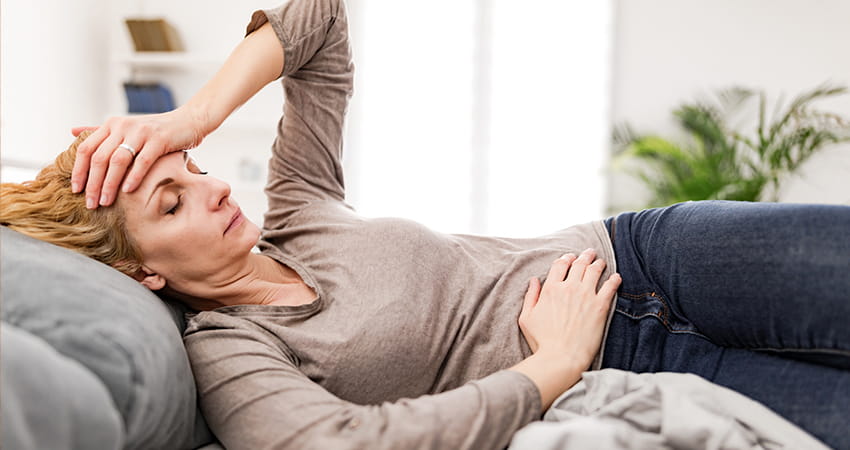 Frau sitzt erschöpft auf dem Sofa – in bestimmten Situationen kann Intervallfasten den Körper zusätzlich belasten.